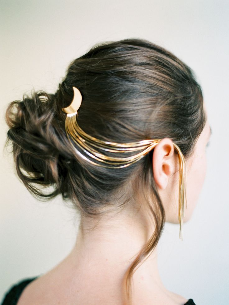 a woman with long dark hair styled in a low bun with a gold crescent moon hair accessory extending down her back. the photo is taken from behind and shows off the intricate details of the hair accessory.
