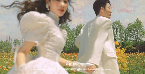 a man and a woman are running handinhand through a field of colorful wildflowers. they are both dressed in elegant white clothing. the woman is wearing a white puffsleeved wedding gown. the man is wearing a white suit jacket and white pants. the background is a hazy blue sky with puffy white clouds. this image has a soft, warm, and romantic feel.