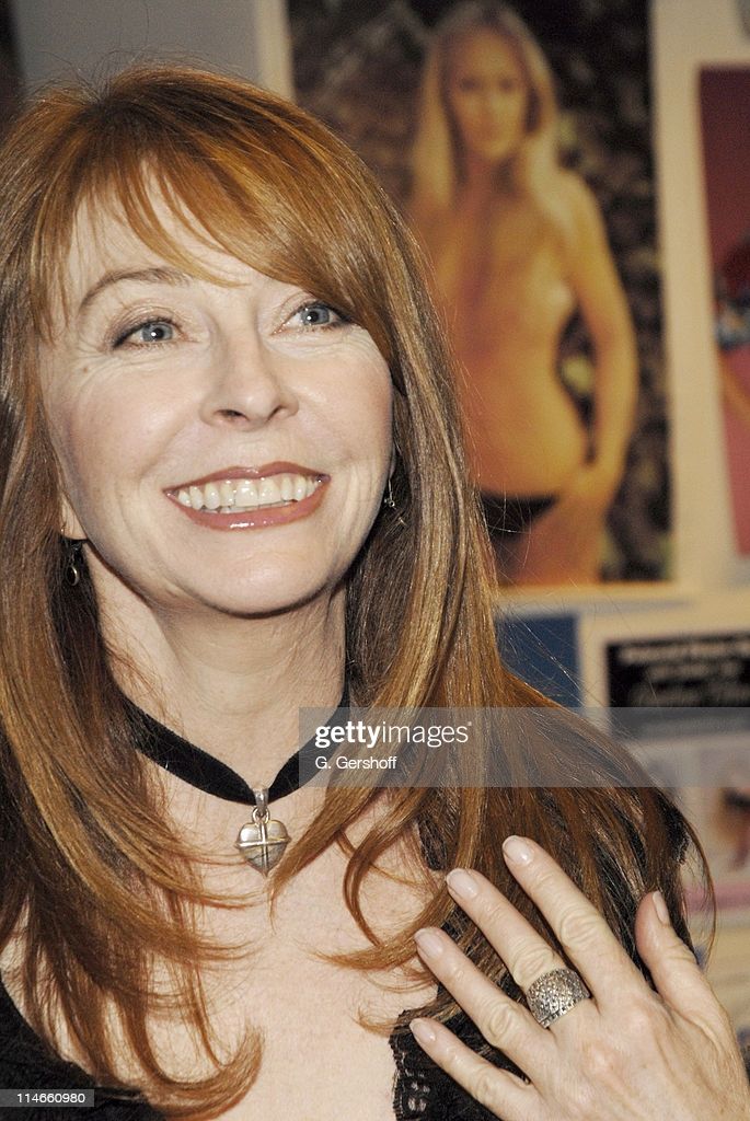 a closeup portrait of a woman with long, red hair. she is wearing a black choker necklace and a ring on her finger. she is smiling and looking at the camera.