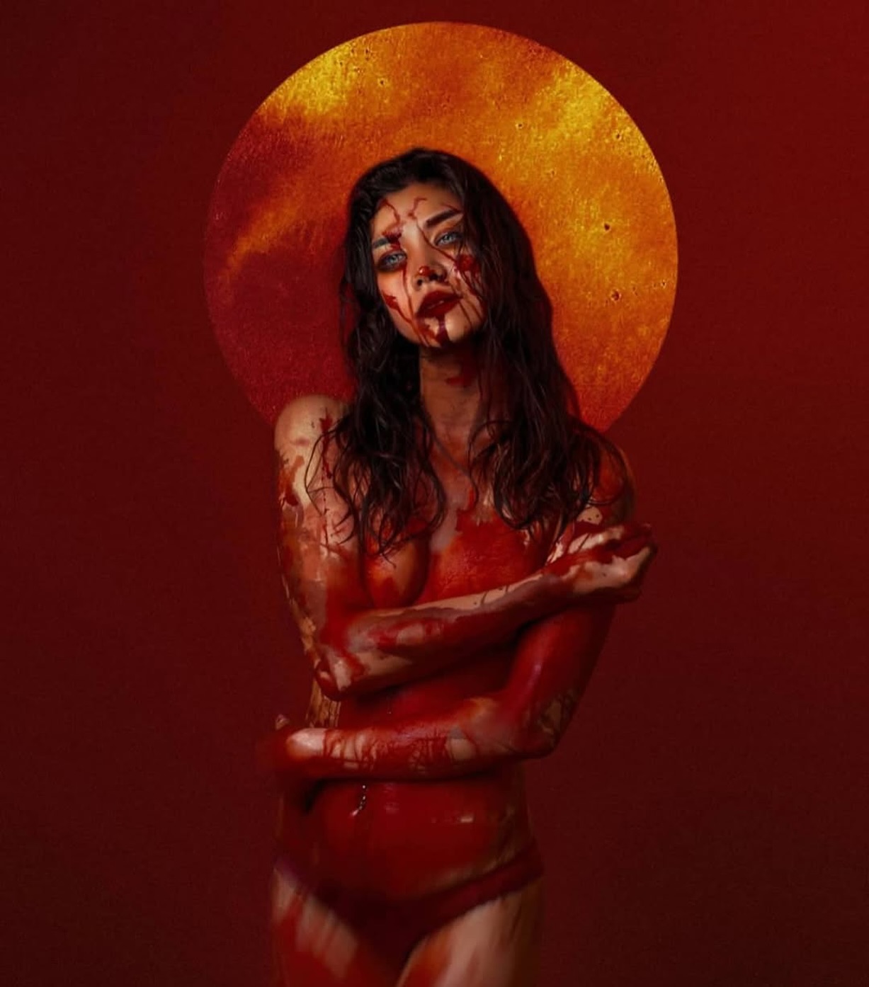 the image is a striking portrait of a young woman covered in what appears to be blood.  her body is mostly naked, with the blood creating a visceral, textured effect on her skin.  her expression is serious and intense, her gaze directed slightly away from the camera.  she is framed by a large, circular, orangegold background that resembles a halo or sun, creating a dramatic contrast against her bloodsoaked form. the overall mood is dark, dramatic, and slightly unsettling, suggesting themes of sacrifice, violence, or possibly religious symbolism. the red tones dominate the image, enhancing the feeling of intensity and creating a powerful visual effect.  the image's style suggests fine art photography or a promotional piece for a horror film or dark fantasy genre.