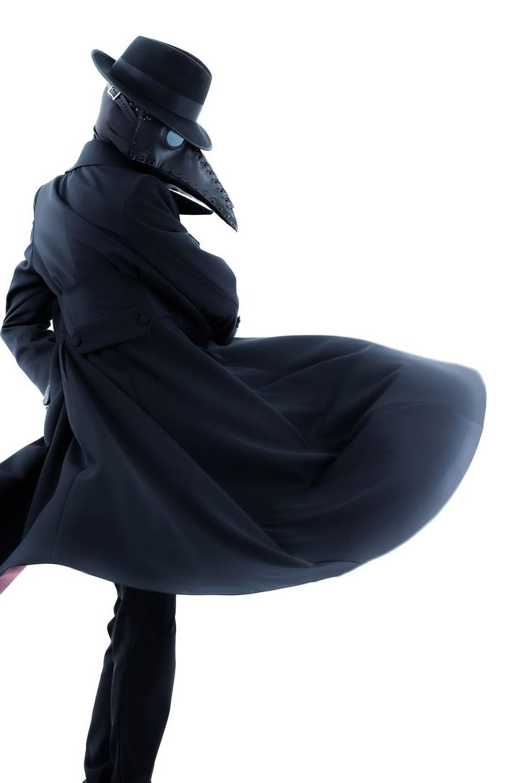 a man in a full plague doctor costume stands against a white background with his coat billowing out behind him. his mask is clearly visible and he wears a black coat and hat.