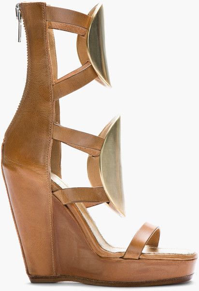 closeup view of a pair of women's tan leather wedge sandals. the sandals feature gold metallic crescentshaped accents on the straps and a high wedge heel. the sandals have multiple straps that crisscross around the ankle and foot, providing support and a unique design. the leather appears to be of high quality, and the overall style is elegant and sophisticated.  the background is plain white, allowing the shoes to stand out prominently.