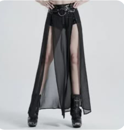 a woman is wearing a black, long, sheer skirt and posing for the camera in a studio. she is looking at the camera. the skirt is very sheer and shows the woman's legs through it. she has on a black belt with metal accents.