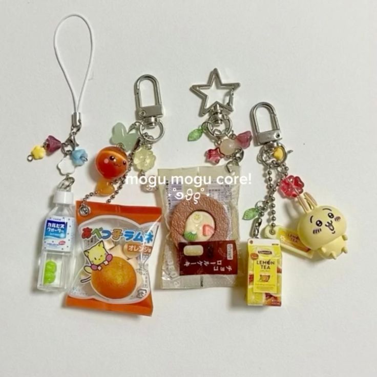the image shows a collection of handmade keychains, each featuring miniature replicas of various snacks and drinks, arranged on a white surface. there are keychains that include a bottle of calpis, a package of orangeflavored candy, a chocolate cake, a box of lemon tea, and a rabbit figurine. each keychain also has additional decorative elements like colorful beads and charms.