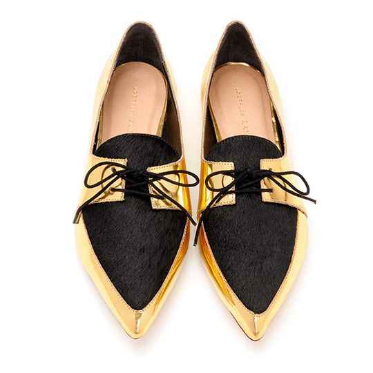 the image shows a pair of women's shoes. they are pointedtoe loafers or oxfords with a unique design. the shoes are primarily gold metallic leather, but feature a central panel of black haironhide material. the shoes have decorative laces that are tied in a bow. the brand name "jessica buurman" (or a similar name) is visible inside the shoes.  the shoes are displayed against a plain white background.