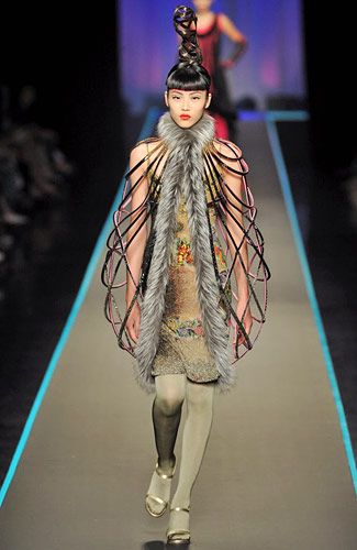 a woman in a glamorous outfit walks down a runway during a fashion show. she has an elaborate hairstyle and is wearing a unique dress with intricate details. she is also wearing stunning accessories. she is looking at the camera with a confident expression, as if she is enjoying the moment.