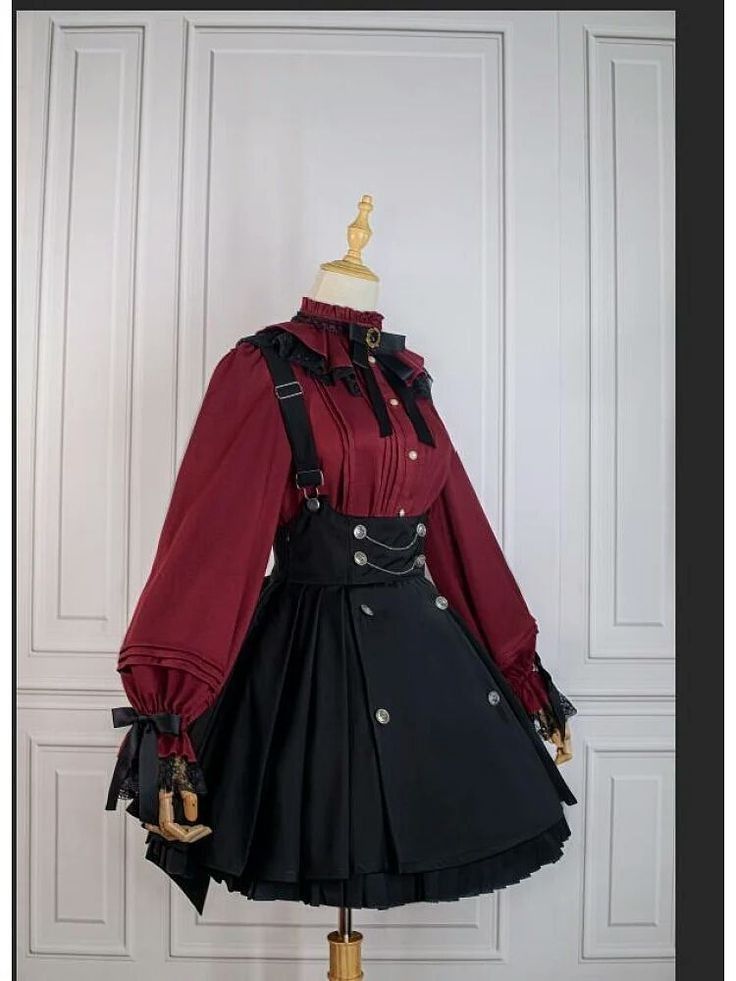 an outfit displayed on a mannequin. the outfit consists of a burgundy longsleeved blouse with ruffled collar and cuffs, accented with black lace and ribbons. the skirt is black, pleated, and has a suspender style with silver buttons and a draped chain.
