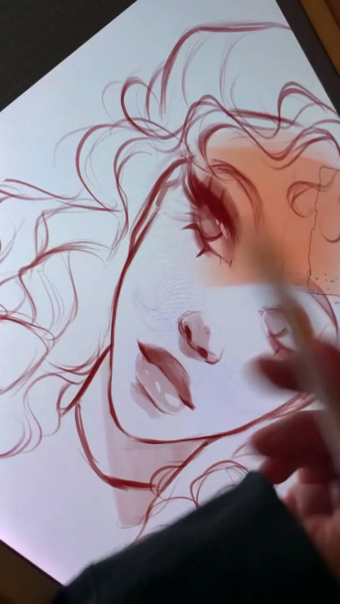 a hand is sketching a woman's portrait. the woman has long, wavy hair. the sketch is drawn in red. the artist is in the process of shading the woman's face. the image is captured from a closeup perspective, focusing on the drawing process.