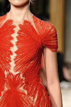 a woman is wearing a beautiful red lace dress. the dress is very elegant and the woman looks very confident and sophisticated. she is standing in front of a blurred background. the dress is made of a delicate lace fabric that is very detailed. the woman's hair is pulled back from her face and she is wearing makeup. the dress is fitted to her body, but it is still flowy and elegant.