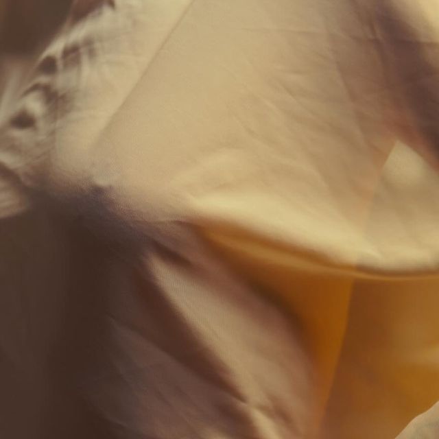 a close up of a smooth and soft beige fabric with a slight gold sheen. the fabric is draped and folded in a way that shows off its texture. the lighting is soft and warm, highlighting the fabric's subtle beauty.