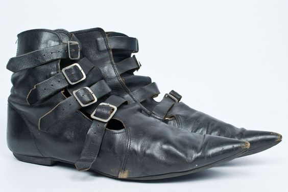 a pair of black leather boots with multiple buckles and pointy toes are positioned against a white background.