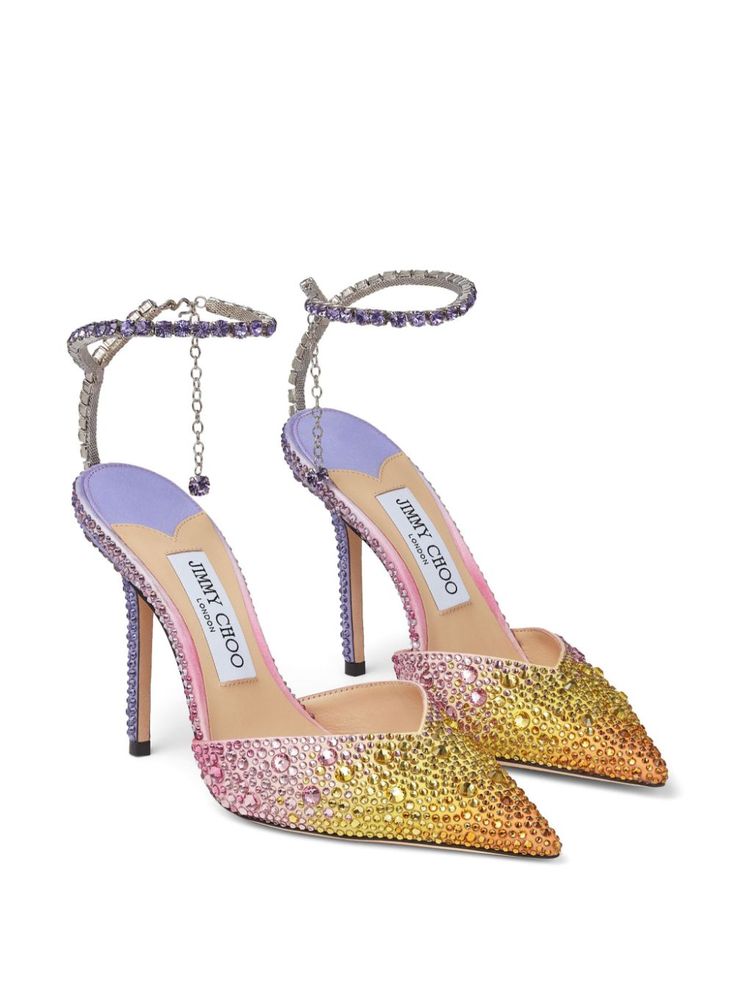 a pair of jimmy choo women's high heels are showcased in a product shot.  the shoes are pointedtoe pumps with stiletto heels and a delicate ankle strap adorned with crystals. the crystals are arranged in an ombre effect, transitioning from purple to pink and then yellow and gold. the shoes have a luxurious and glamorous appearance, suitable for special occasions or bridal wear.  the jimmy choo branding is visible on the insole.