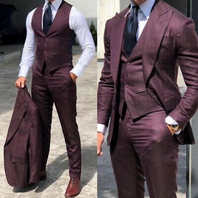 the image shows two men in maroon suits. the man on the left is wearing a vest and dress shirt with trousers and dress shoes. he's holding the suit jacket in his hand. the man on the right is wearing the full suit with a tie.