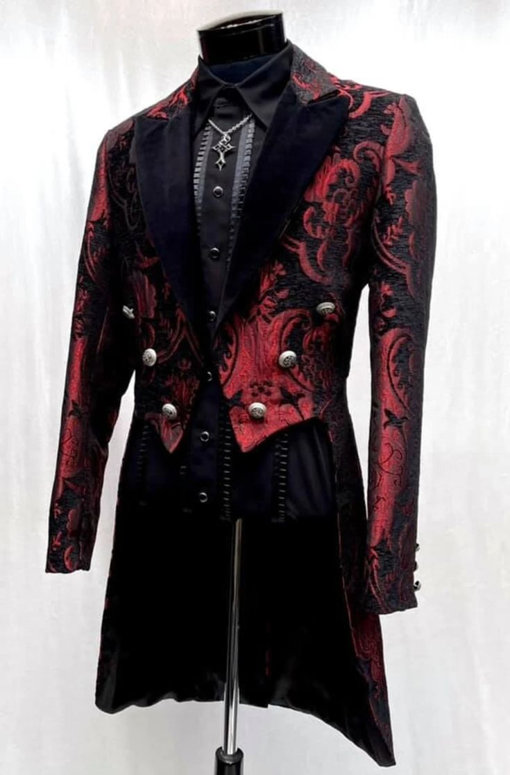 a red and black patterned tailcoat over a black shirt and cross necklace is on display on a mannequin. the tailcoat has velvet lapels and silver buttons. the background is a plain white fabric.