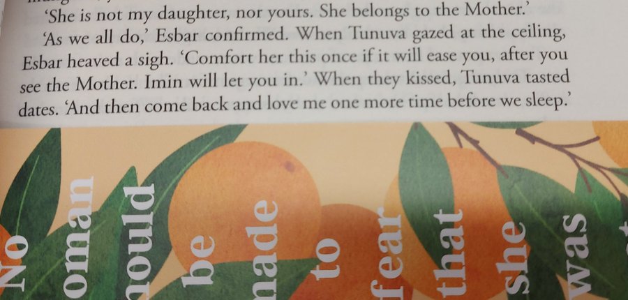 the image shows a closeup of a book page with text on top, and a book cover design featuring oranges and leaves at the bottom. the text on the page includes dialogue between characters named esbar, tunuva, and imin, with references to "the mother". the typography on the book cover is visible through the orange and leaf design, creating a visually appealing effect.