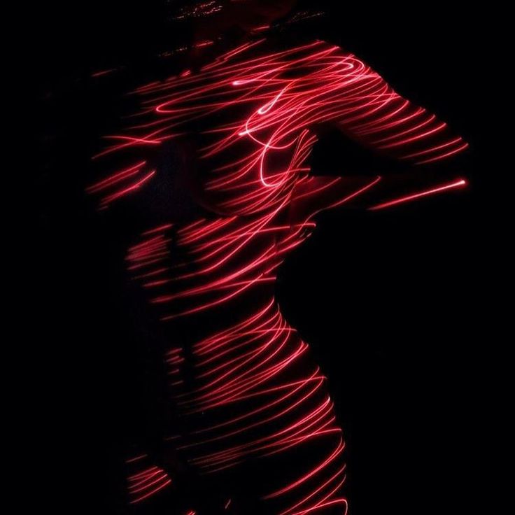 the image is a striking piece of light art.  a female figure's silhouette is captured in neartotal darkness, outlined and draped with vibrant, swirling lines of red laser light. the light trails create an abstract and ethereal effect, obscuring much of the body's detail while still suggesting the form's curves. the contrast between the dark background and the bright red light is very powerful, making the figure the central focus of the image.  the overall mood is sensual and artistic, suggestive of motion and energy. the photography techniques used appear to be long exposure photography with laser light sources.