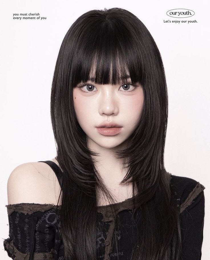 a young woman with long black hair and bangs looks directly at the camera. she is wearing a black and brown  off the shoulder top. the background is white, and the image is lit with soft lighting.  the woman is looking at the camera with a serious expression.