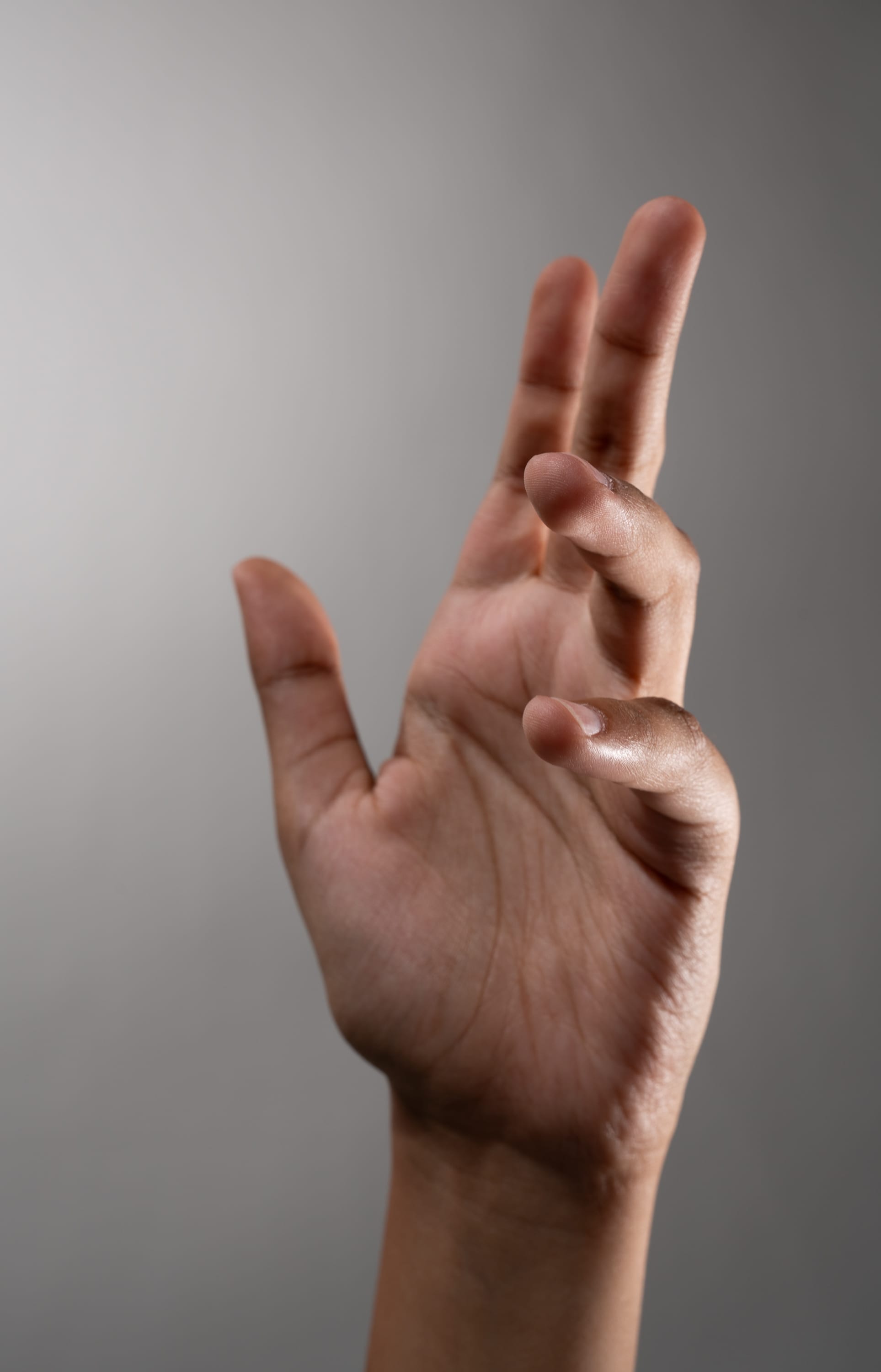 a close up of a hand with brown skin reaching upwards against a light gray background.
