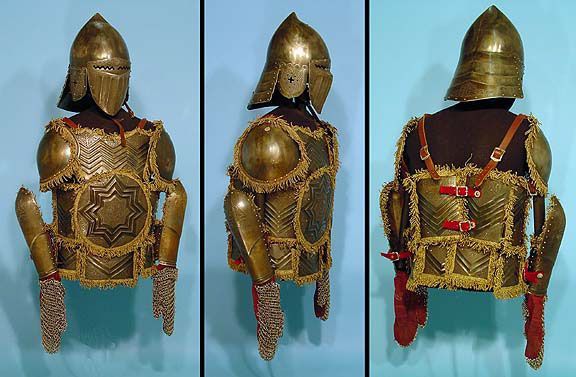 three views of an ornate suit of armor against a light blue background. the armor is made of metal plates and features intricate designs and patterns, possibly of ottoman or turkish origin. the suit includes a helmet with a rounded top and a visor, a breastplate with a starshaped design, shoulder guards, arm guards, gauntlets, and a skirt of chainmail.  the armor is displayed on a mannequin, giving a sense of its size and how it would have been worn.