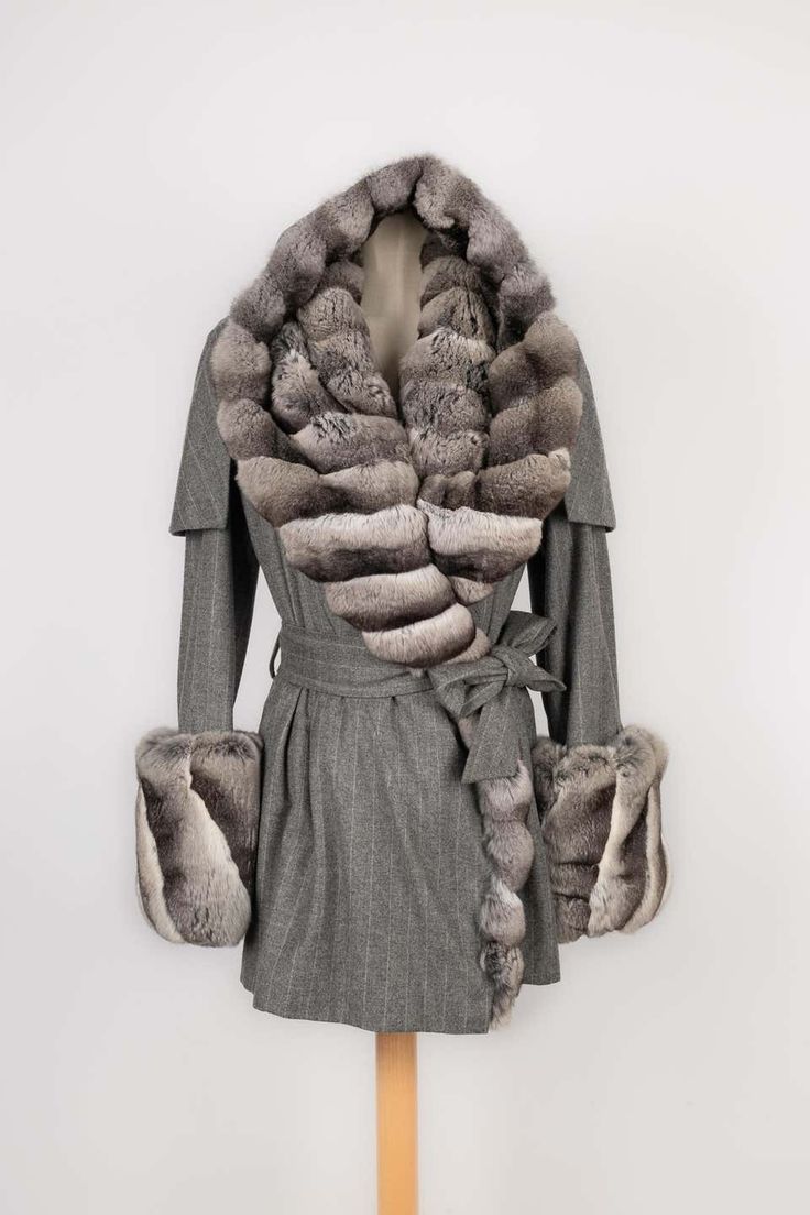 a grey furtrimmed wool coat with a wraparound design and a belt. it features a large fur collar and cuffs. the coat is displayed on a mannequin against a white background.