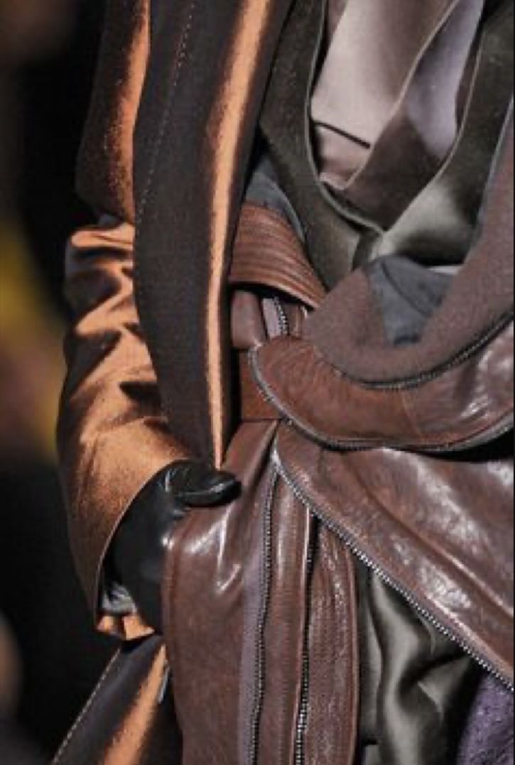 a closeup image of a brown leather jacket. it features a  zipper detailing on the sleeves and body of the jacket. the jacket is stylish and trendy with a casual vibe.
