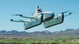 a white flying car with a person inside is hovering in the air against a backdrop of mountains and blue sky. the car has four propellers and a sleek, futuristic design. the image is a representation of the future of transportation.