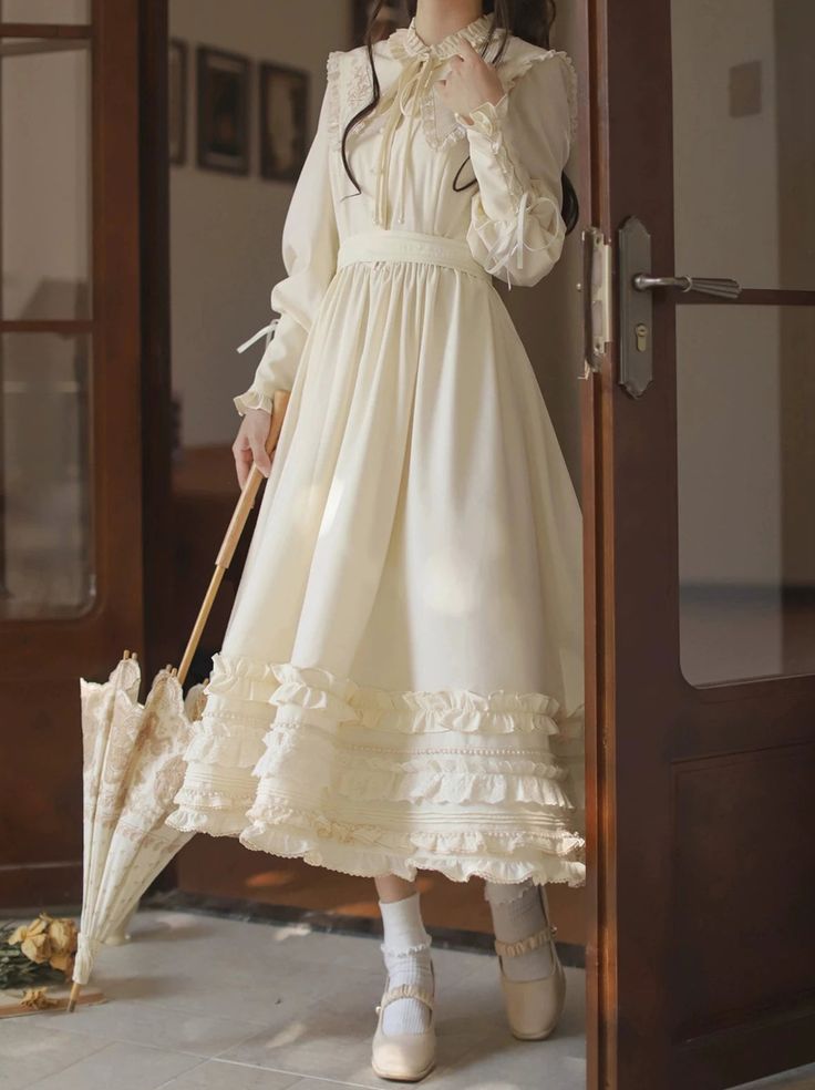 a woman is standing in a doorway, holding a lace parasol.  she is wearing a longsleeved, creamcolored dress with lace trim and ruffles. the dress falls to her ankles, and she is wearing white socks and mary jane shoes. the doorway is made of dark wood, and the walls are painted a light color. the room is welllit, with natural light streaming in from the doorway.