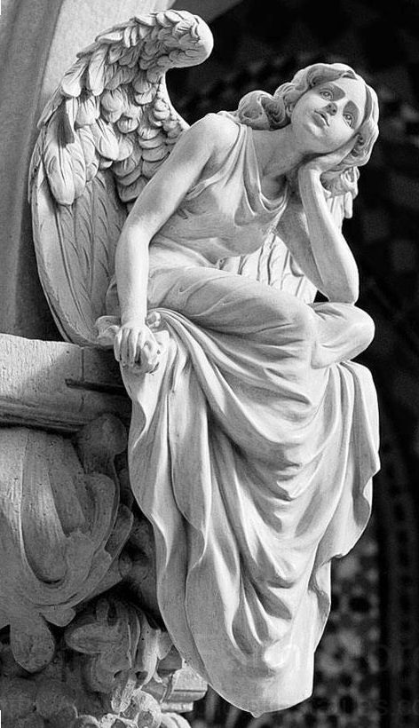 a black and white photograph of a stone sculpture of an angel with wings outstretched. the angel is a female figure, dressed in flowing robes, and is depicted with a sorrowful expression. the sculpture is situated on a stone pedestal and there is foliage in the background.  the sculpture is likely from a cemetery or church.  the image has a vintage feel.