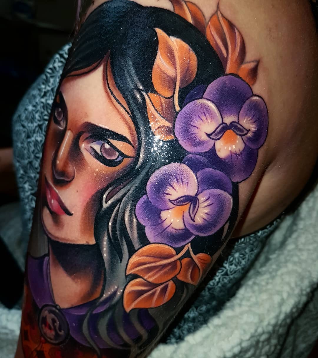 a closeup photograph of a neotraditional tattoo of a woman with dark hair and purple flowers on her shoulder.