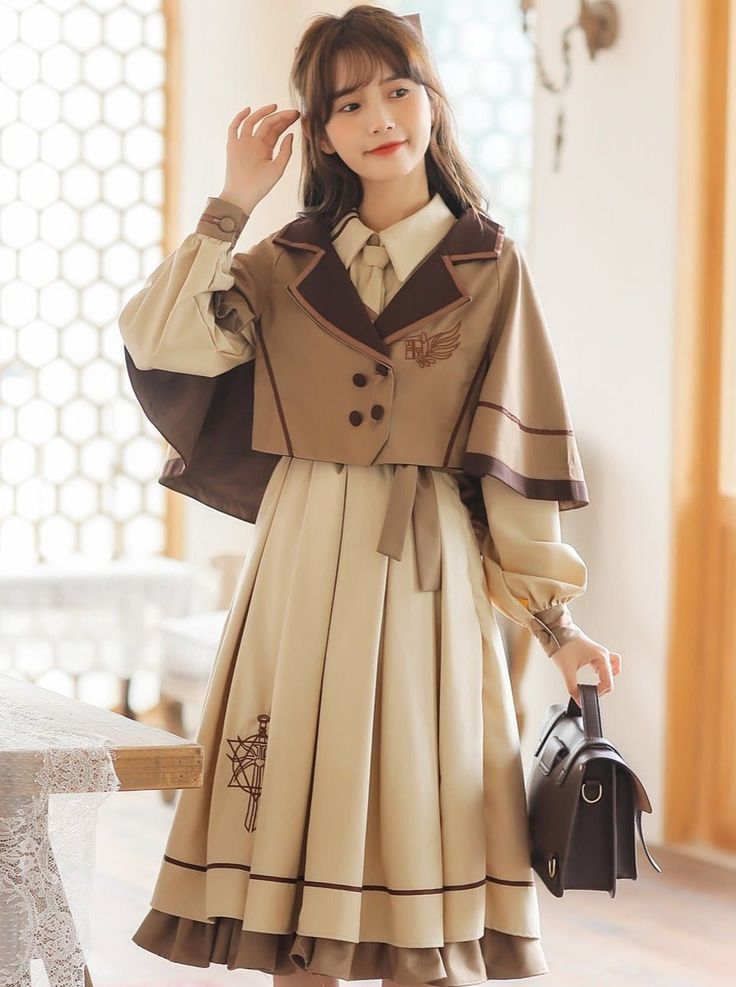 a young asian woman poses in a studio setting, showcasing a stylish lolitainspired outfit. she wears a beige dress with brown accents, a matching capelet, and a white blouse underneath. the dress features intricate embroidery and a flowing skirt. she carries a dark brown satchel and looks effortlessly chic.