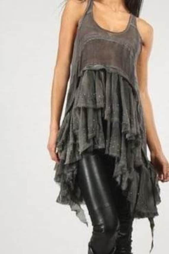 a woman is wearing a stylish grey sleeveless tank top with layers of ruffled fabric. the top is asymmetrical and has a relaxed, casual fit. she is also wearing black leggings and posing for a photoshoot, showcasing the trendy and chic outfit.