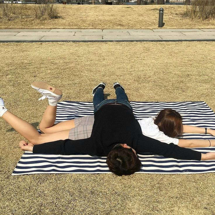 a couple lies on a striped picnic blanket in the grass. they are both smiling and looking very happy together. they are enjoying their time together and are clearly in love.  the image conveys a sense of joy, love, and relaxation.  the couple is dressed in casual clothes and the setting is a sunny park. the image is warm and inviting, making it a perfect representation of a romantic getaway.