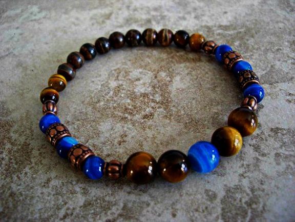 a close up of a blue and brown beaded bracelet on a white surface. the bracelet is made of round tiger's eye beads and blue glass beads. the bracelet is lying flat on the surface.