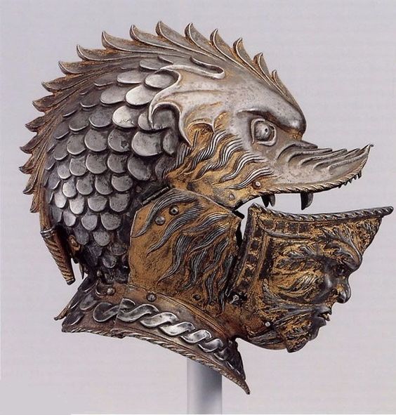 a closeup view of an ornate, silver and gold helmet sculpted into the shape of a dragon's head. the helmet's visor is raised, revealing a sculpted human face underneath.  the detail of the dragon's scales and the intricate design of the helmet are highlighted against a neutral background.