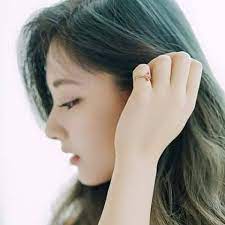 the image shows a closeup portrait of a young asian woman with long, dark hair. her face is turned to the side, and she has a soft, melancholic expression. she is wearing minimal makeup and a simple gold ring. the lighting is soft and natural, highlighting the smooth texture of her skin and hair. the overall tone of the image is serene and feminine.