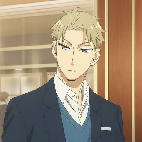 the image shows the upper body of a young man with short blond hair and striking blue eyes. he is dressed in a dark blue suit with a white shirt and a light blue sweater vest. a white rectangular tag is visible on his left lapel. his expression is serious, almost brooding, as he appears to be looking at something or someone in front of him. the setting seems to be an indoor location, likely an office or a formal setting, with a warm, soft light illuminating the scene.