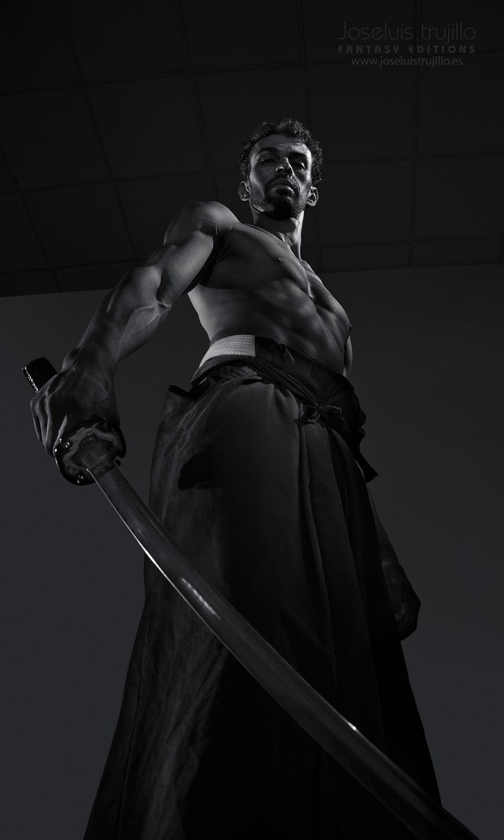 a muscular man in a samuraiinspired outfit holding a katana, against a dark backdrop. the image is black and white and shot in a lowkey style, creating a dramatic and intense atmosphere. the man's serious expression and the sharp lines of his sword create a sense of power and focus. the image is an artistic representation of strength and determination.