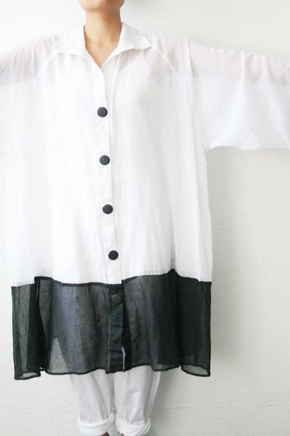 a person is wearing a white buttondown shirt with a black sheer bottom. the shirt is oversized and has short sleeves. the person is also wearing white pants.
