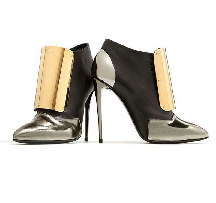 the image shows a pair of women's highheeled ankle boots.  the boots are predominantly black leather but feature a silver metallic toe and heel cap, along with a striking gold metal accent panel on the side of each boot.  the heels are thin stilettos, and the boots have a pointed toe. the shoes appear to be made of highquality materials and have a sophisticated, fashionable design. one boot is slightly angled forward, while the other is positioned behind it to display both the profile and front view.  the background is plain white to emphasize the shoes.
