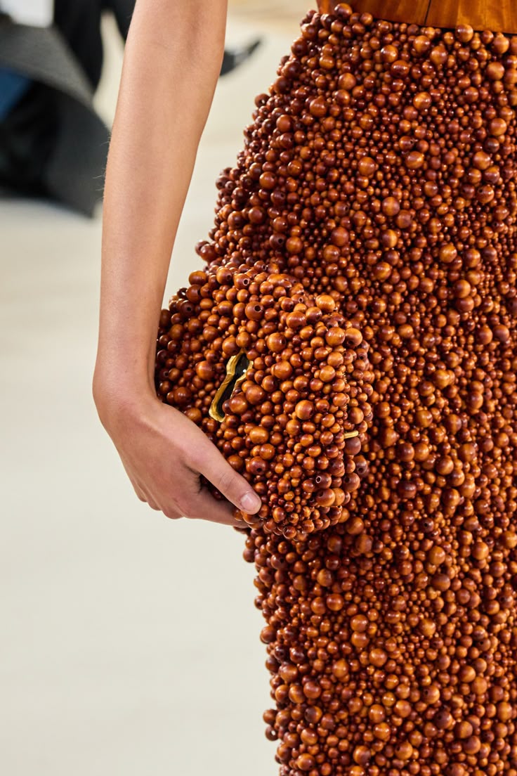 a closeup shot shows a woman holding a beaded clutch bag, with her beaded dress visible in the background. the items are covered in brown beads.