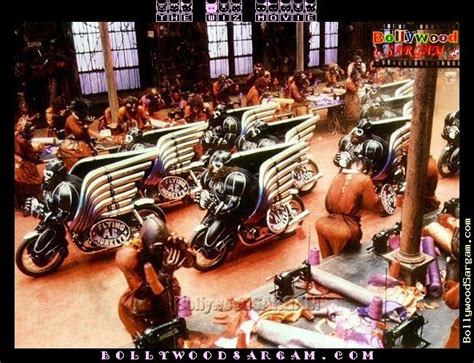 this is a picture of the set for a bollywood film. several people in costume are seated on custommade motorcycles. the motorcycles are adorned with leather and chrome and have large, silver wings.  the scene appears to be set on a city street at night, with a sense of excitement and energy present.  the people are posing and interacting with the camera, capturing a sense of artistic dynamism. the image has a vibrant and captivating appeal, conveying a sense of spectacle and grandeur associated with bollywood productions.