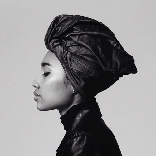 a black and white side profile portrait of a woman wearing a headwrap. she has closed eyes and smooth skin. she is also wearing a leather jacket with a turtleneck. the image has a confident and elegant feel.