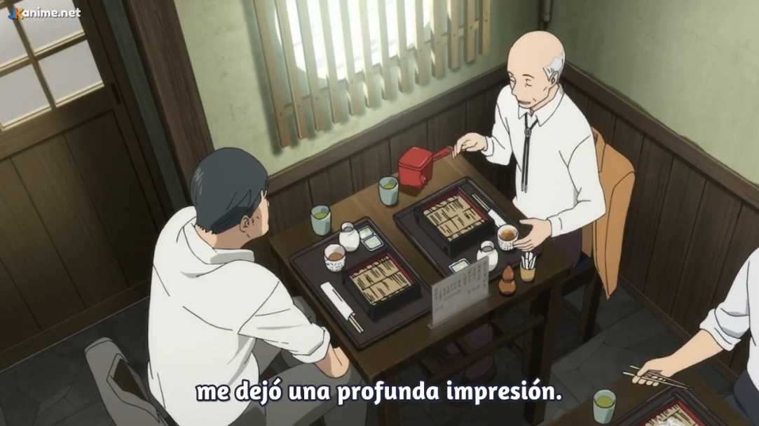 a still image from what appears to be an anime, depicting two men having a meal at a restaurant. the scene is from a high angle, looking down at the table where the two men are seated. the man on the left, with dark hair, is listening intently to the older, bald man on the right, who is pouring tea. the table is set with bowls of soba noodles and teacups. the restaurant has a traditional japanese aesthetic, with wooden furniture and bamboo accents. the atmosphere is calm and inviting.