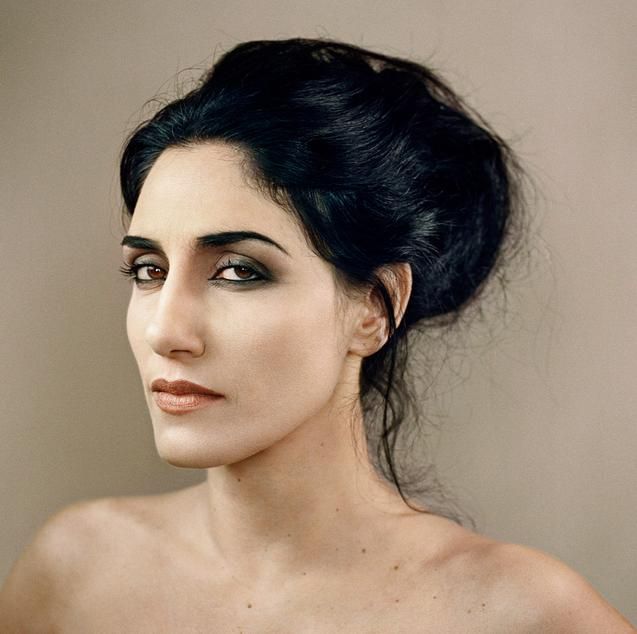 a closeup portrait of a woman with dark hair styled in an updo, wearing dark eyeshadow and lipstick, against a neutral background, showcasing fine art photography aesthetics.