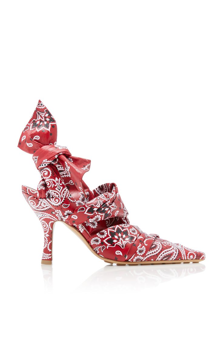 a pair of red high heels with a bandana print. the shoes have a pointed toe, ankle strap, and a stiletto heel. they are a designer shoe and are perfect for a party or special occasion.