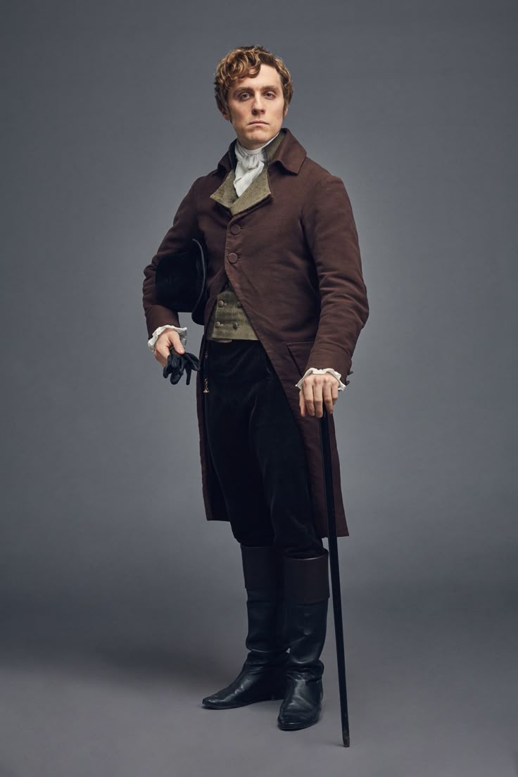 a man dressed in regency era clothing stands for a fullbody portrait. he wears a brown coat, dark pants, and black riding boots. he is holding a hat and gloves in one hand and leaning on a cane with the other. his coat is open, revealing a light green vest and a white frilled shirt. the background is a plain gray color.