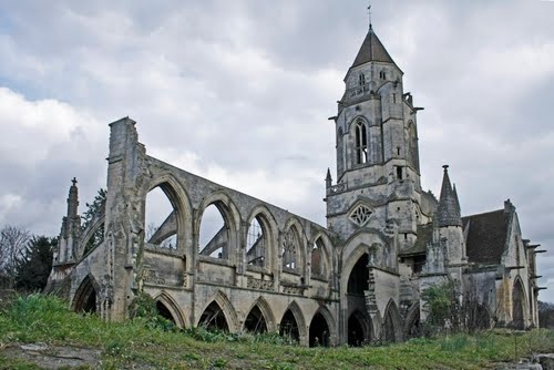 he image shows the ruins of a large stone church or abbey.  the architecture is gothic in style, characterized by pointed arches and a tall, slender tower.  much of the structure is in a state of disrepair, with walls missing and roofs collapsed.  the stone is weathered and aged, showing the effects of time and decay.  the foreground is covered in green grass, and an overcast sky hangs above. the overall impression is one of history, age, and the passage of time.