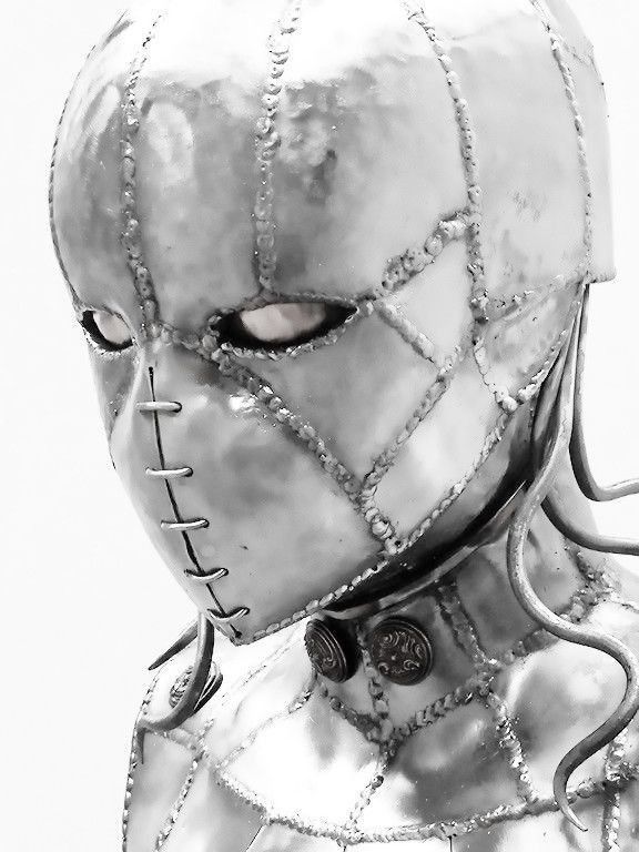 a close up view of a silver robot sculpture with a face, showing only the top of the head, with the silver mask covering most of the face, the metal head is made to look like stitches are holding it together.