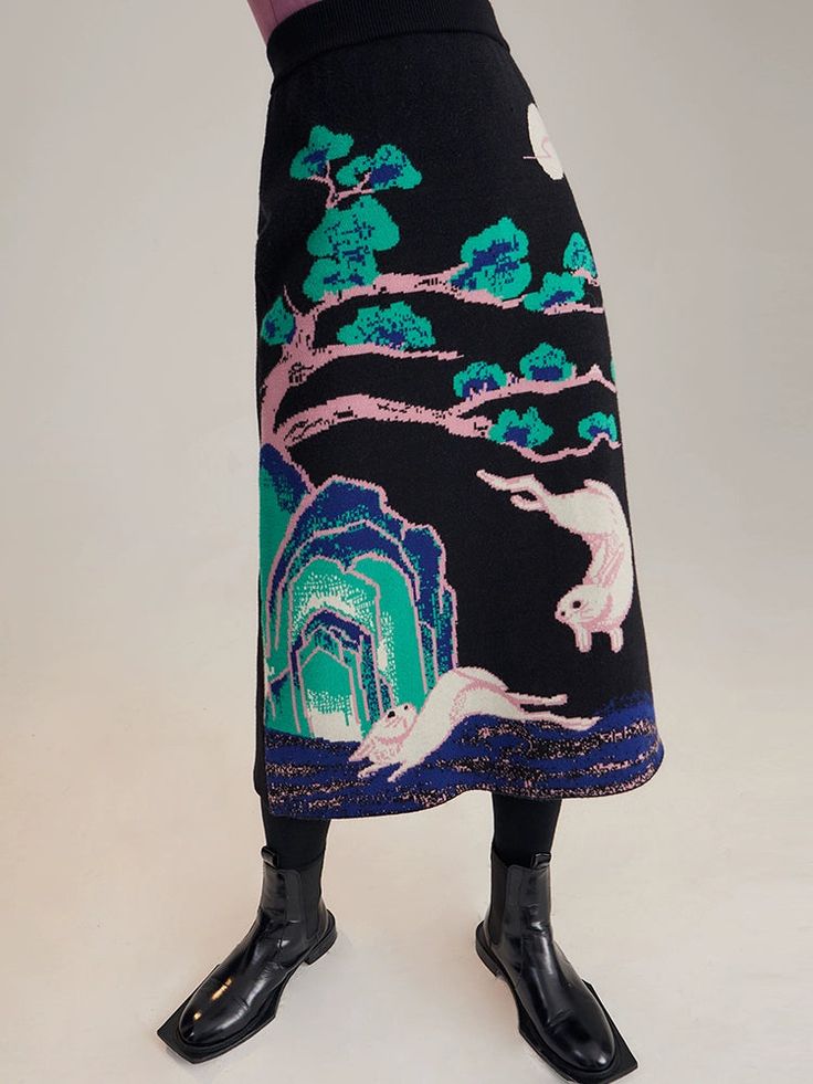 a woman is standing wearing a black skirt with a floral pattern and black ankle boots. she is standing in front of a white background.