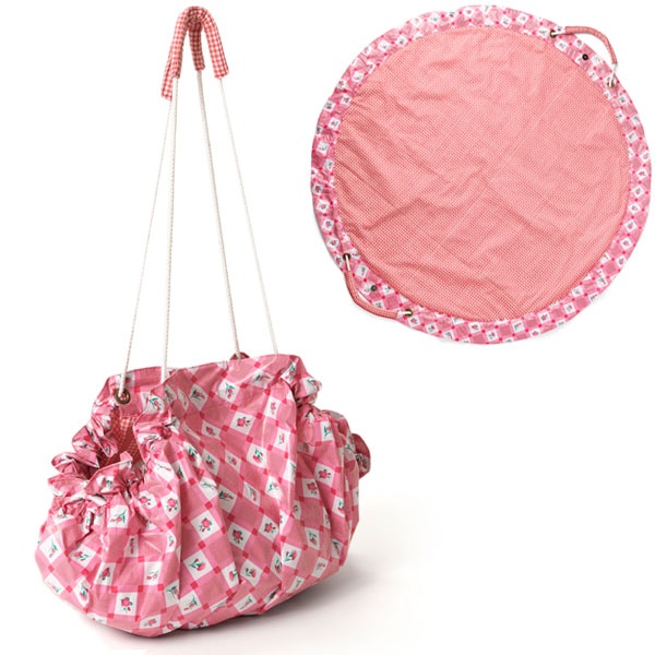 the image shows a pink drawstring bag with a checkered and floral pattern, alongside a matching play mat. the bag has a handle and appears to be used for toy storage.
